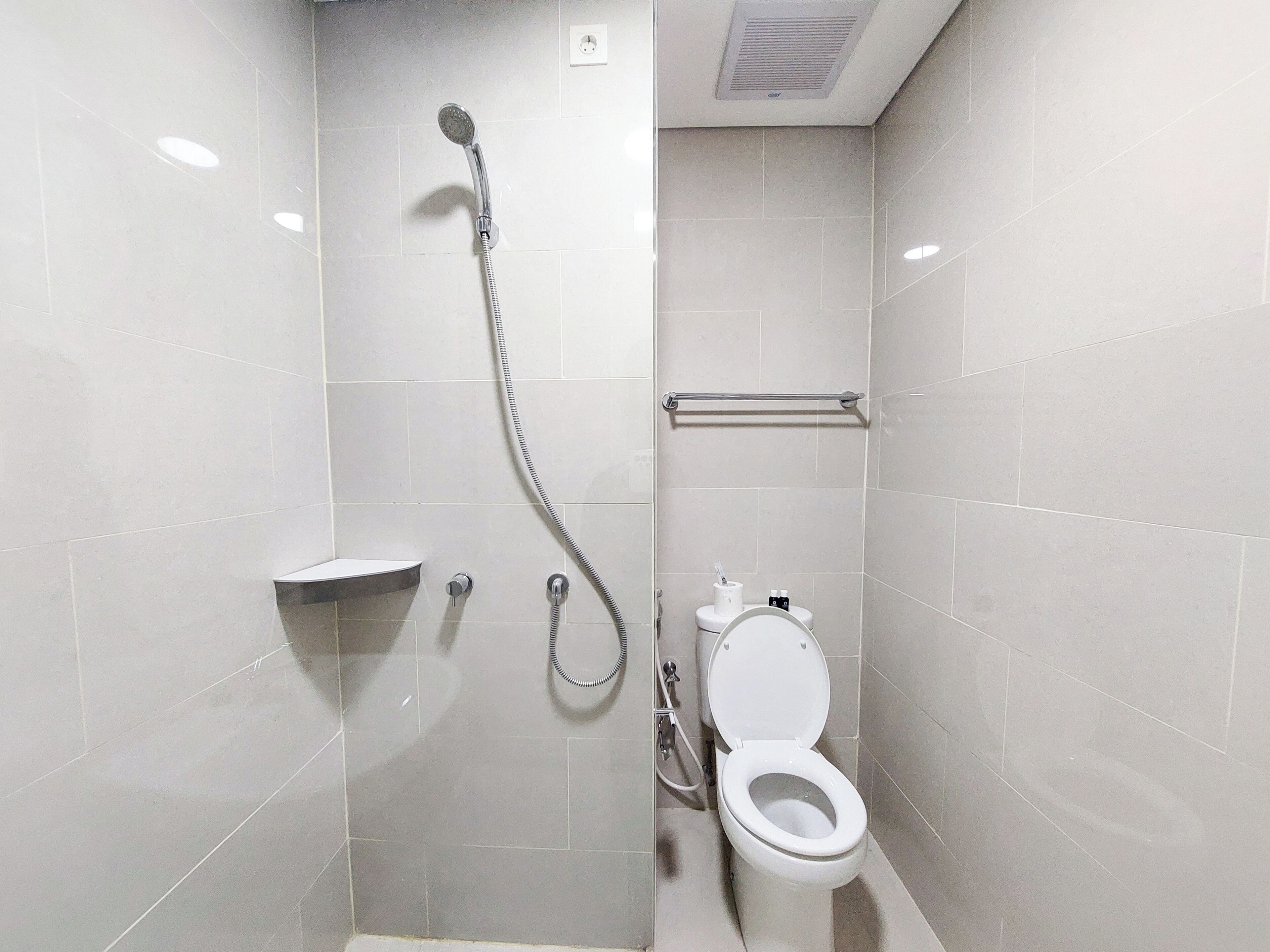 Une petite salle de bain moderne, équipée d’une douche, de toilettes et d’une étagère.