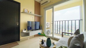 Een woonkamer met een televisie, een plant en uitzicht op een stadsgezicht.