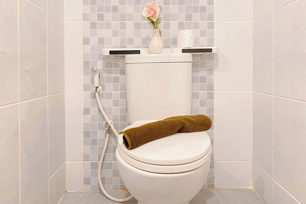 A toilet with a towel on the seat, a vase with a flower, and a toilet paper holder.