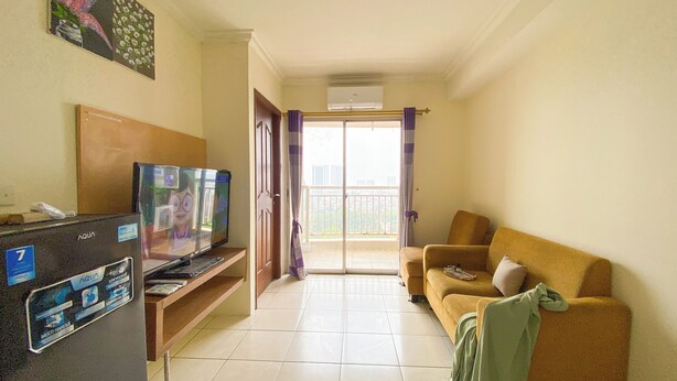 A living room with a TV, a sofa, and a balcony with curtains. - Comfortable and Restful 2BR at Great Western Apartment (Tangerang)