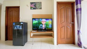 A living room with a television on a stand, a refrigerator, and two wooden doors. - Comfortable and Restful 2BR at Great Western Apartment (Tangerang)