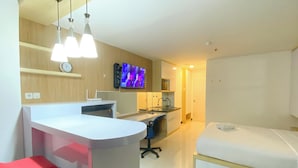 Une chambre d’hôtel moderne équipée d’une kitchenette, d’une télévision, d’un fauteuil rouge et d’un lit.