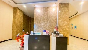 Un comptoir d’accueil avec un mur en marbre en arrière-plan, un panneau indiquant le service à la clientèle et une plante en pot.