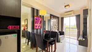 A modern dining area with a black table and chairs, a yellow pendant light, and a large window with a view of greenery. - Modern Look 1BR Apartment at Silkwood Residence (Tangerang)
