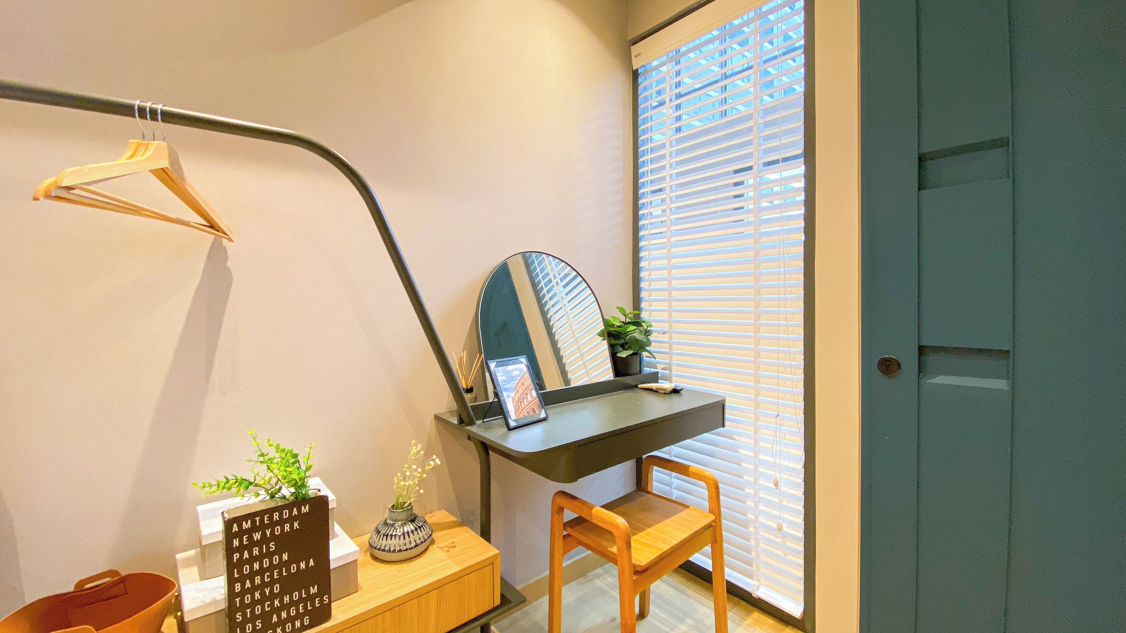A small workspace with a desk, chair, and a mirror. There's a potted plant on the desk and a sign listing cities.