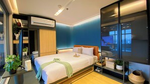 A modern hotel room with a large bed, a built-in wardrobe, an air conditioning unit, and a large window offering a view of the city. - Elegant 2BR Loft Garden Villa at Collins Boulevard Apartment (Tangerang)