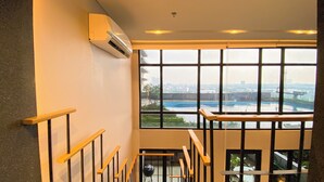 A staircase with wooden handrails leading to an upper floor, a large window with a view of a river and cityscape, and an air conditioning unit mounted on the wall. - Elegant 2BR Loft Garden Villa at Collins Boulevard Apartment (Tangerang)