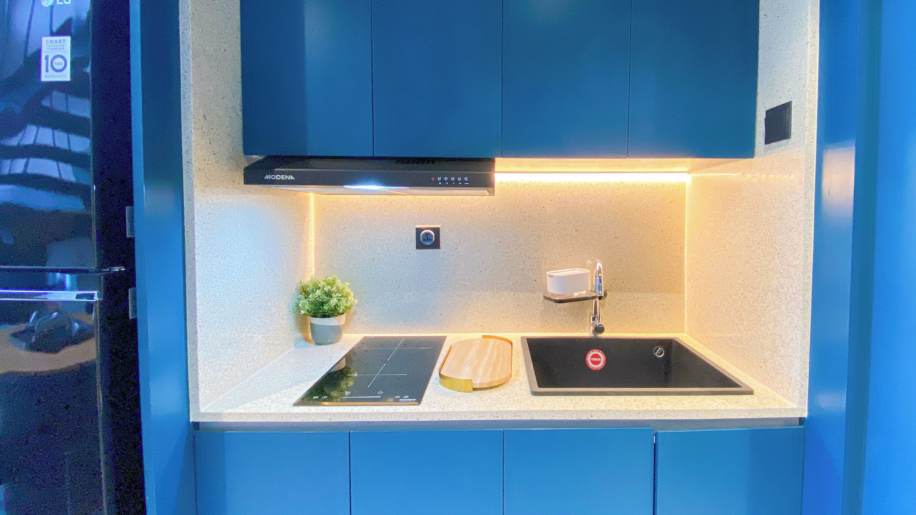 Una cucina moderna con pensili blu, una cappa aspirante nera, un piano cottura a induzione integrato, un tagliere di legno e una piccola pianta in vaso.