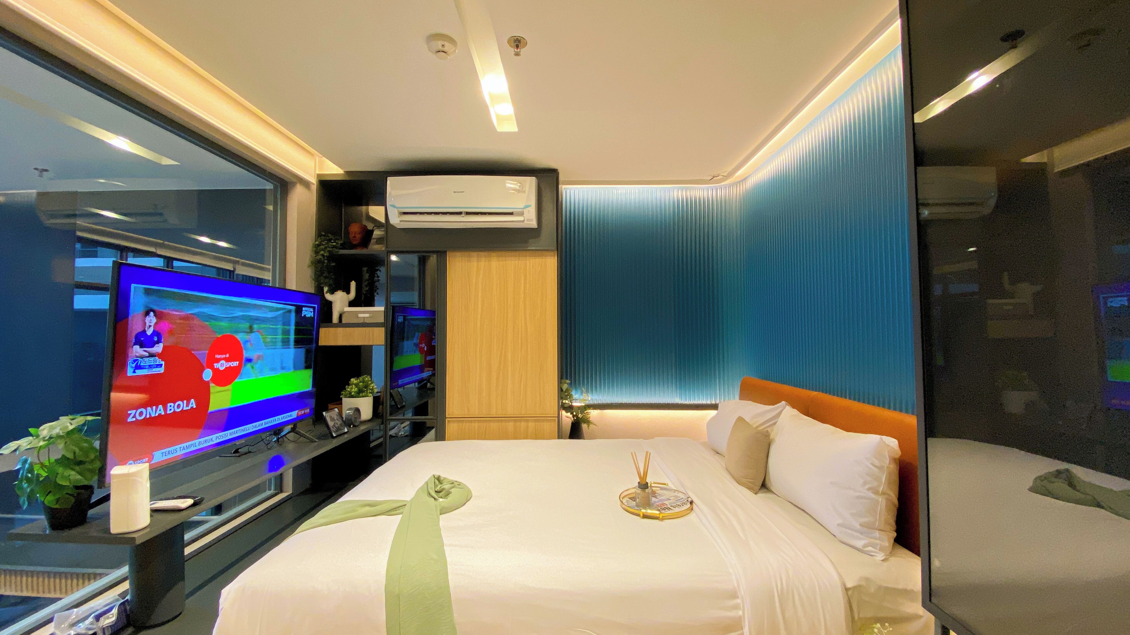 Ein modernes Hotelzimmer mit einem großen Bett, einem Flachbildfernseher und einem Fenster mit blauen Vorhängen.