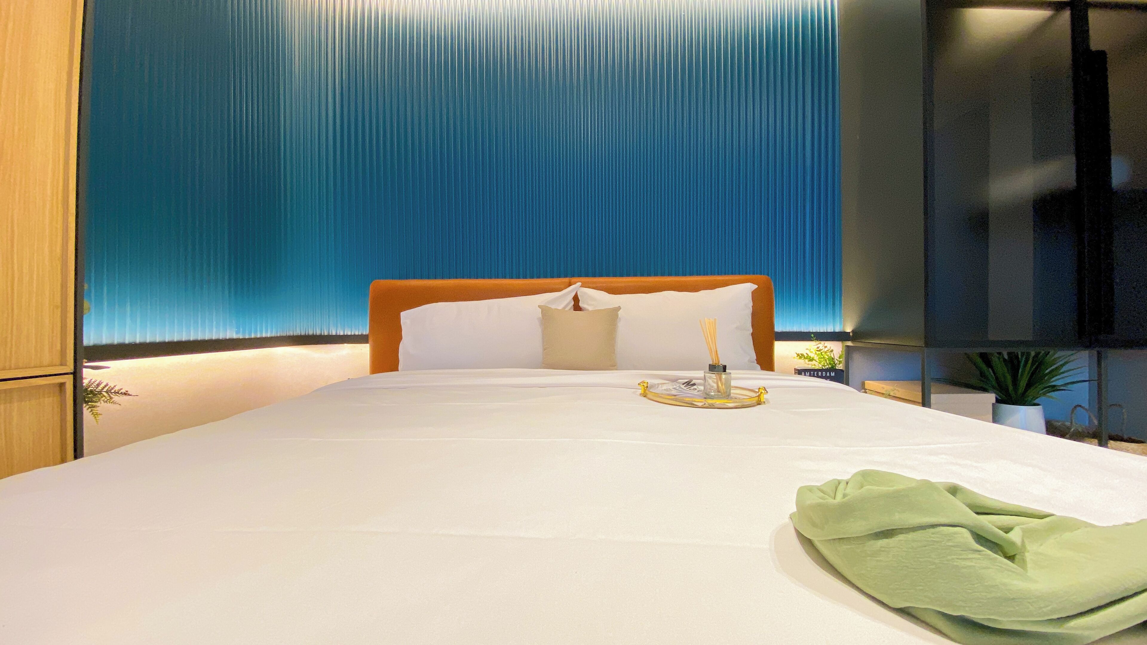 A neatly made bed with white linens, a wooden headboard, and a green throw.
