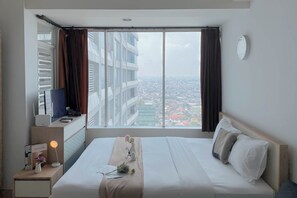A hotel room with a large window, a bed, a bedside table with a lamp, and a view of the cityscape.