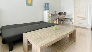 Una habitación con un sofá negro, una mesa de madera, un dispensador de agua y una puerta con un respiradero.