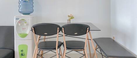 A compact room with a kitchenette, a water dispenser, two chairs, a small table, and a potted plant.