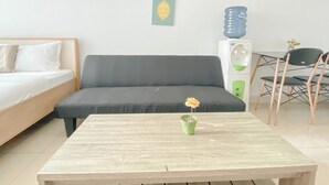 Una habitación con una cama, un sofá, una mesita con una flor, un dispensador de agua y una silla.