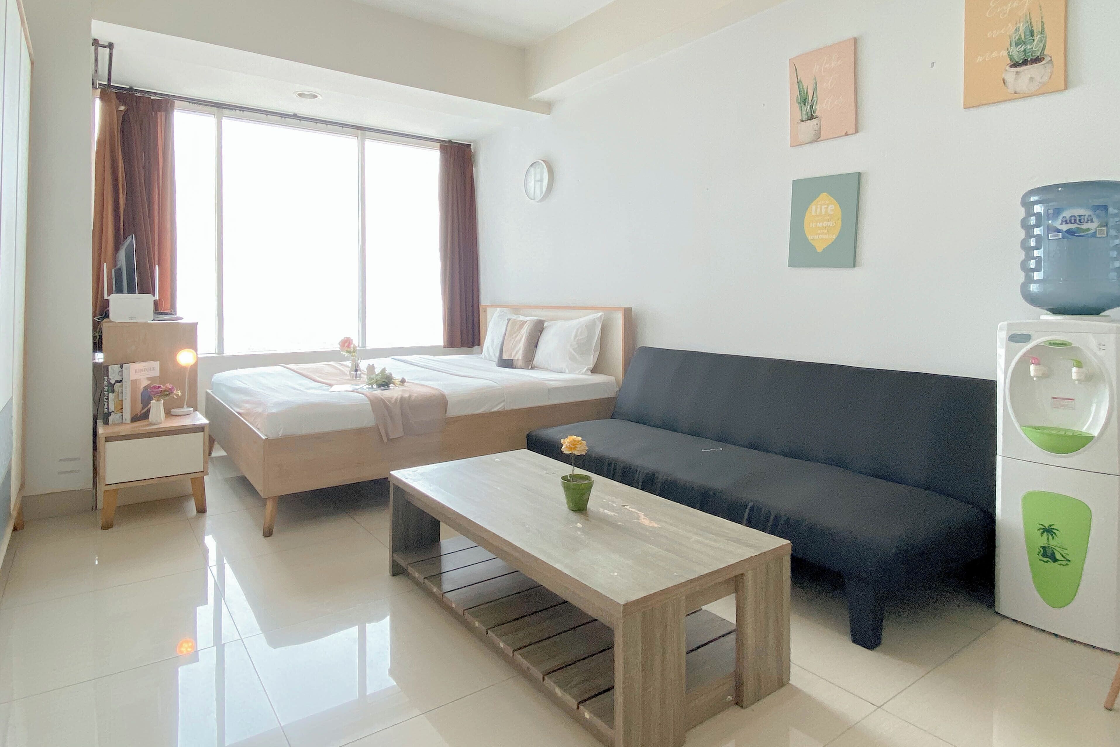 Una habitación luminosa con cama, sofá, una mesa de centro y dispensador de agua.