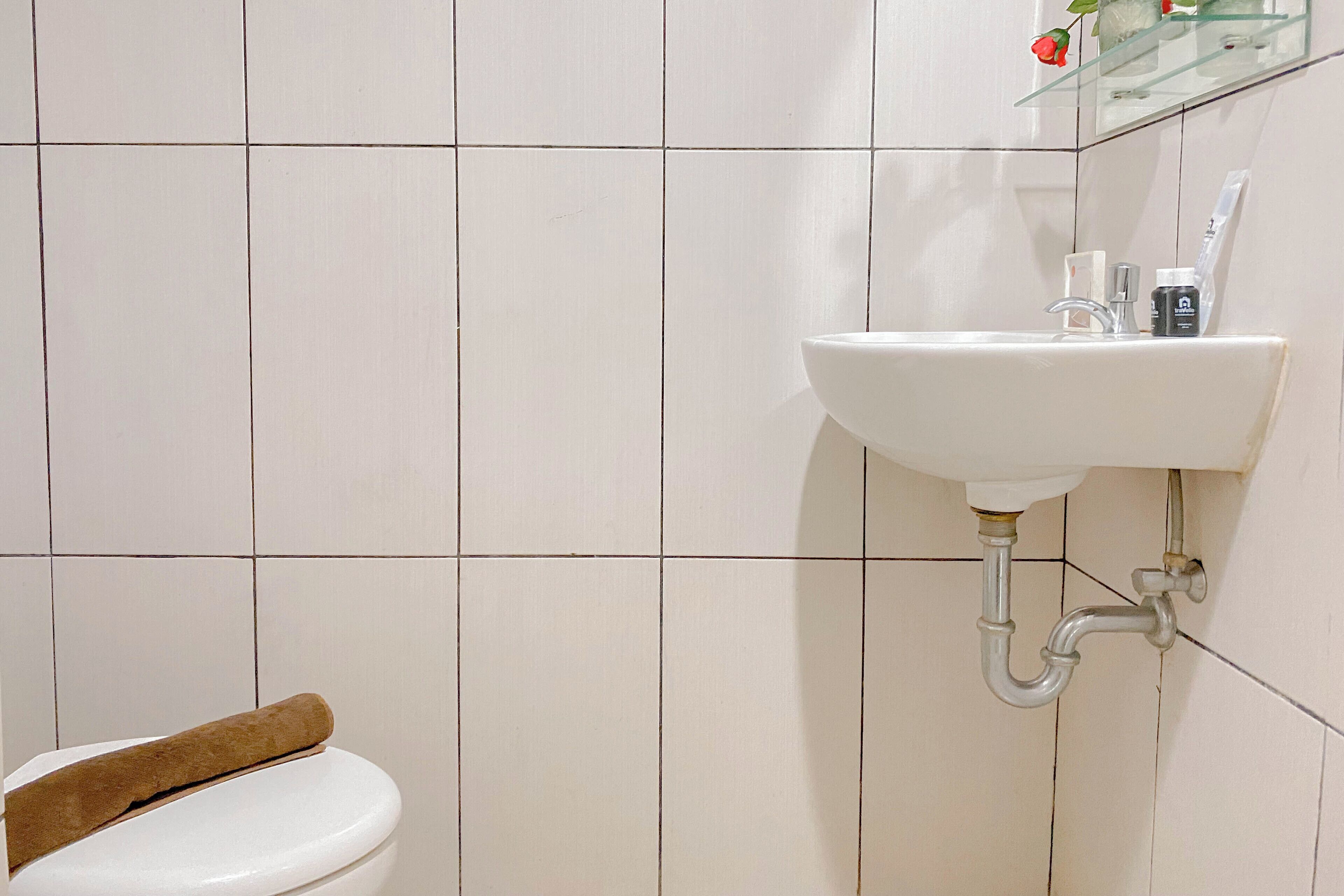 A bathroom with a white toilet, a white sink with a mirror above it, and a glass shelf with toiletries.