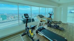 A gym with cardio machines and a large window with a city view. - Cozy Studio at Grand Kamala Lagoon Apartment near Mall (Bekasi)
