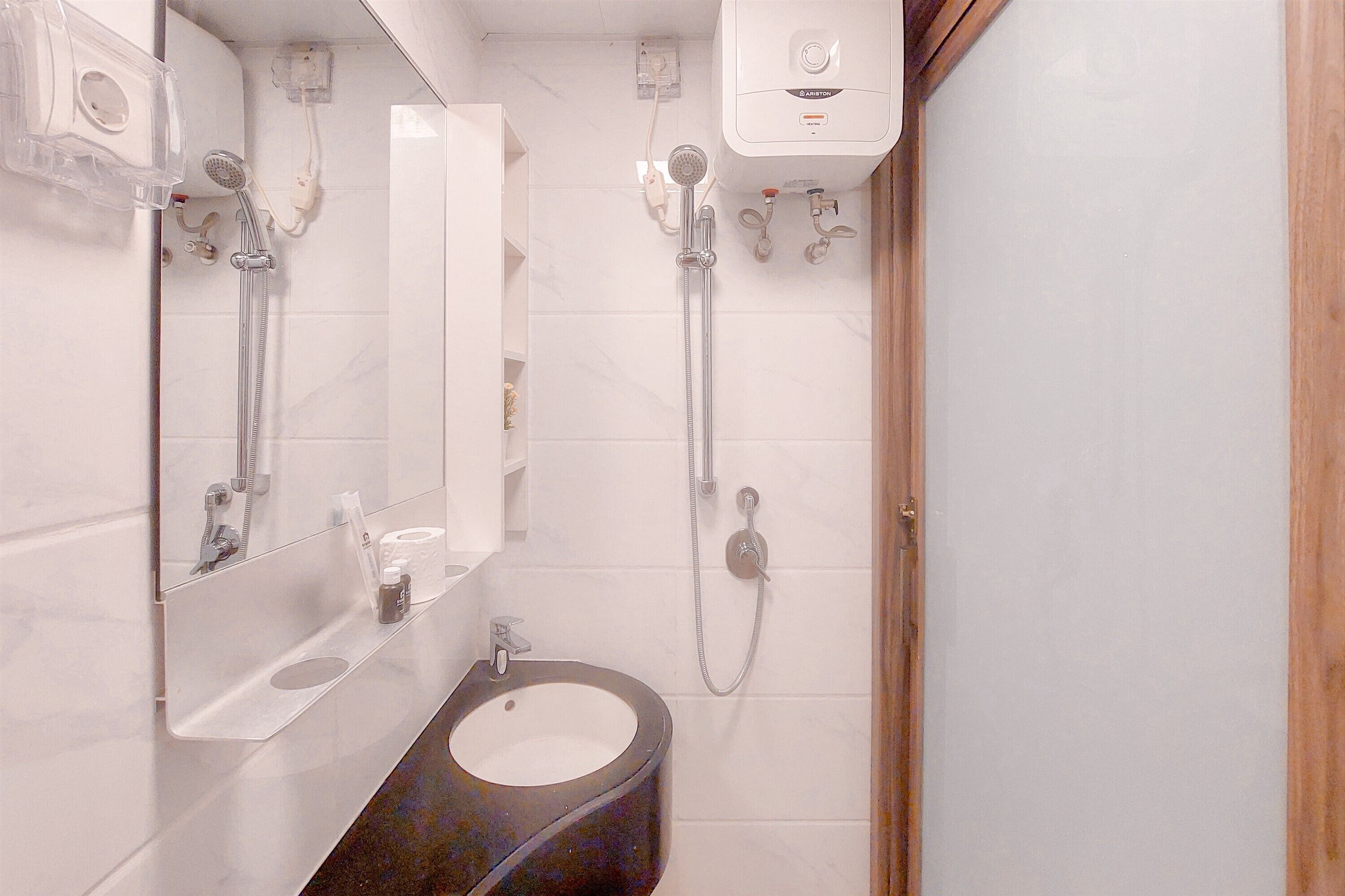 Ein modernes Badezimmer mit integriertem Waschbecken, einem Spiegel, einer Handbrause und einem an der Wand befestigten Toilettenpapierhalter.