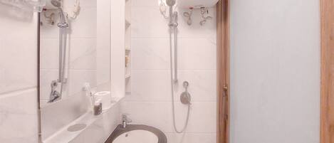 Ein modernes Badezimmer mit integriertem Waschbecken, einem Spiegel, einer Handbrause und einem an der Wand befestigten Toilettenpapierhalter.