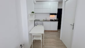 Una cocina compacta con gabinetes blancos, una pequeña mesa de comedor y una silla.