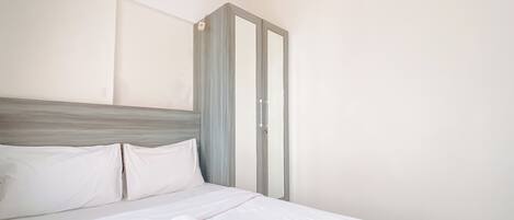 A neatly made bed with white linens and rolled towels, a grey headboard, and a grey wardrobe with a white door.