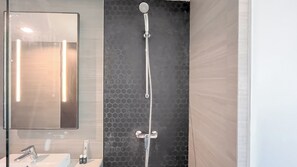 A modern bathroom with a glass shower enclosure, a large mirror, and a sink with toiletries. - Studio Skales Residence Near Segara Water Sports Bali (Nusa Dua)