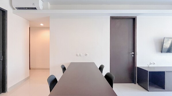Un salón de conferencias con una larga mesa, cuatro sillas, una puerta y un escritorio pequeño con un monitor.