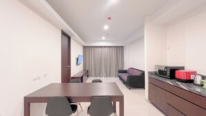 A modern hotel room with a dining area, a sofa, a TV, and a kitchenette. - Luxurious 2BR (No Kitchen) Apartment at Skales Residence Nusa Dua Bali (Nusa Dua)