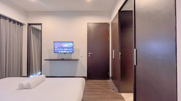 Une chambre d’hôtel avec un lit, un téléviseur posé sur un meuble, une porte et une fenêtre avec des rideaux.