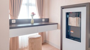 Una camera moderna con scrivania integrata, un piccolo sgabello, una finestra con tende e un quadro elettrico a parete.