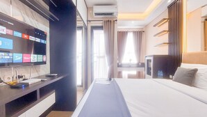 Camera d'albergo con una grande TV a schermo piatto che mostra diverse piattaforme di streaming, un letto con lenzuola bianche, una scrivania con un portatile e altri dispositivi elettronici, e una finestra con tende.