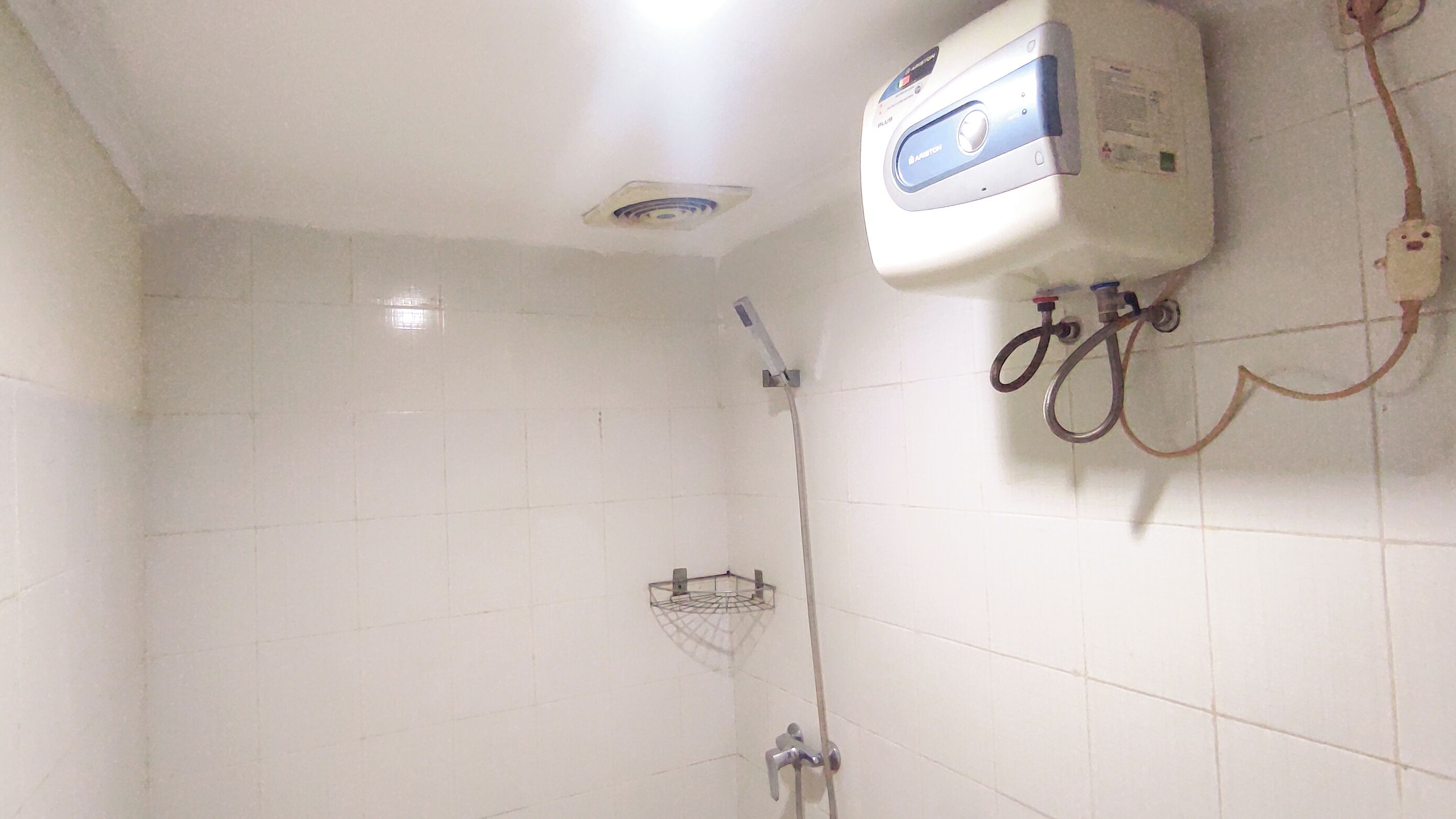 A bathroom with white tiled walls, a shower with a handheld showerhead, and a wall-mounted water heater.
