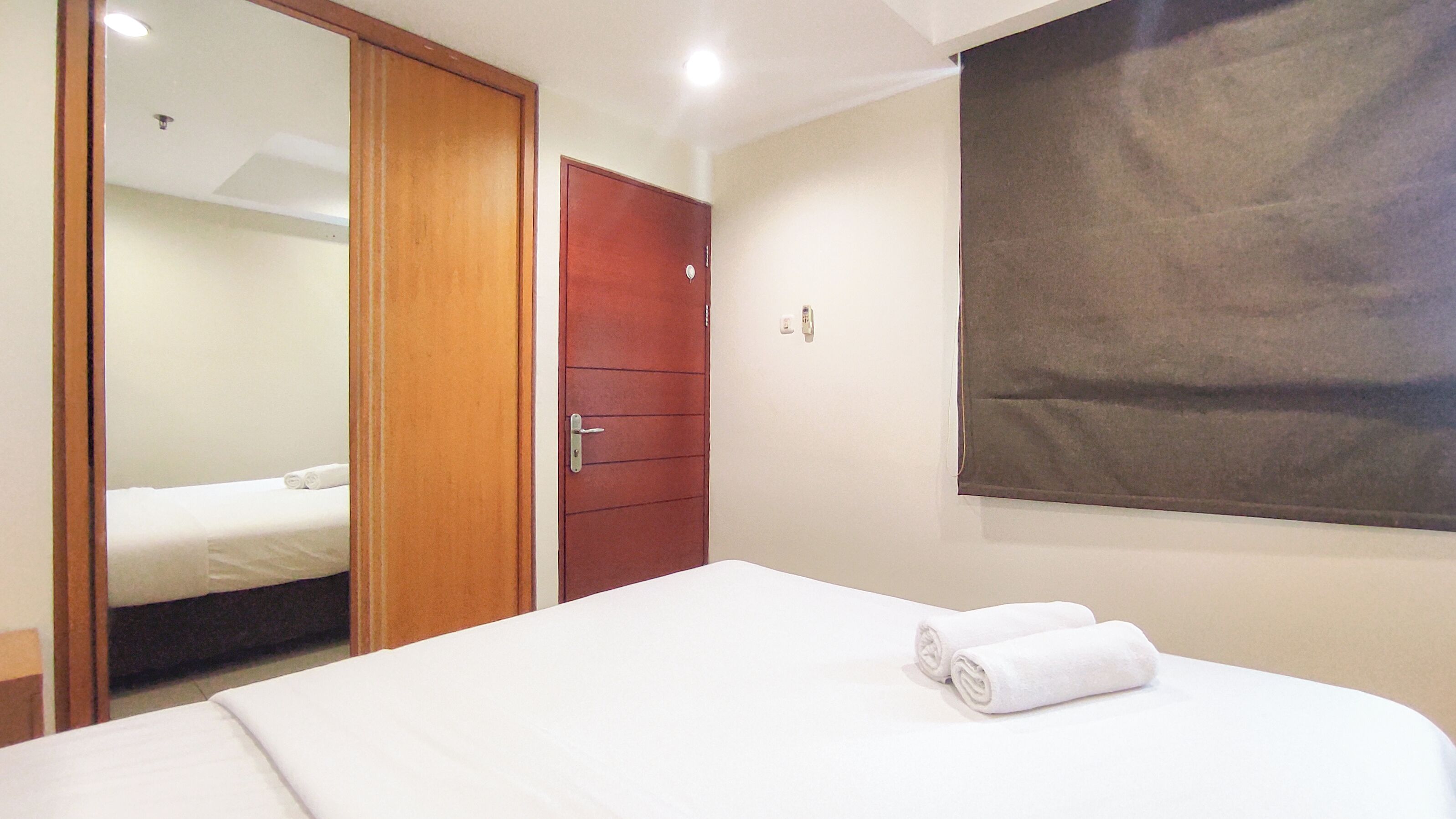 A hotel room with a bed, a wooden wardrobe, and a large window with a brown blind.