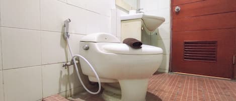 A toilet with a bidet attachment in a bathroom with tiled walls and a red door.