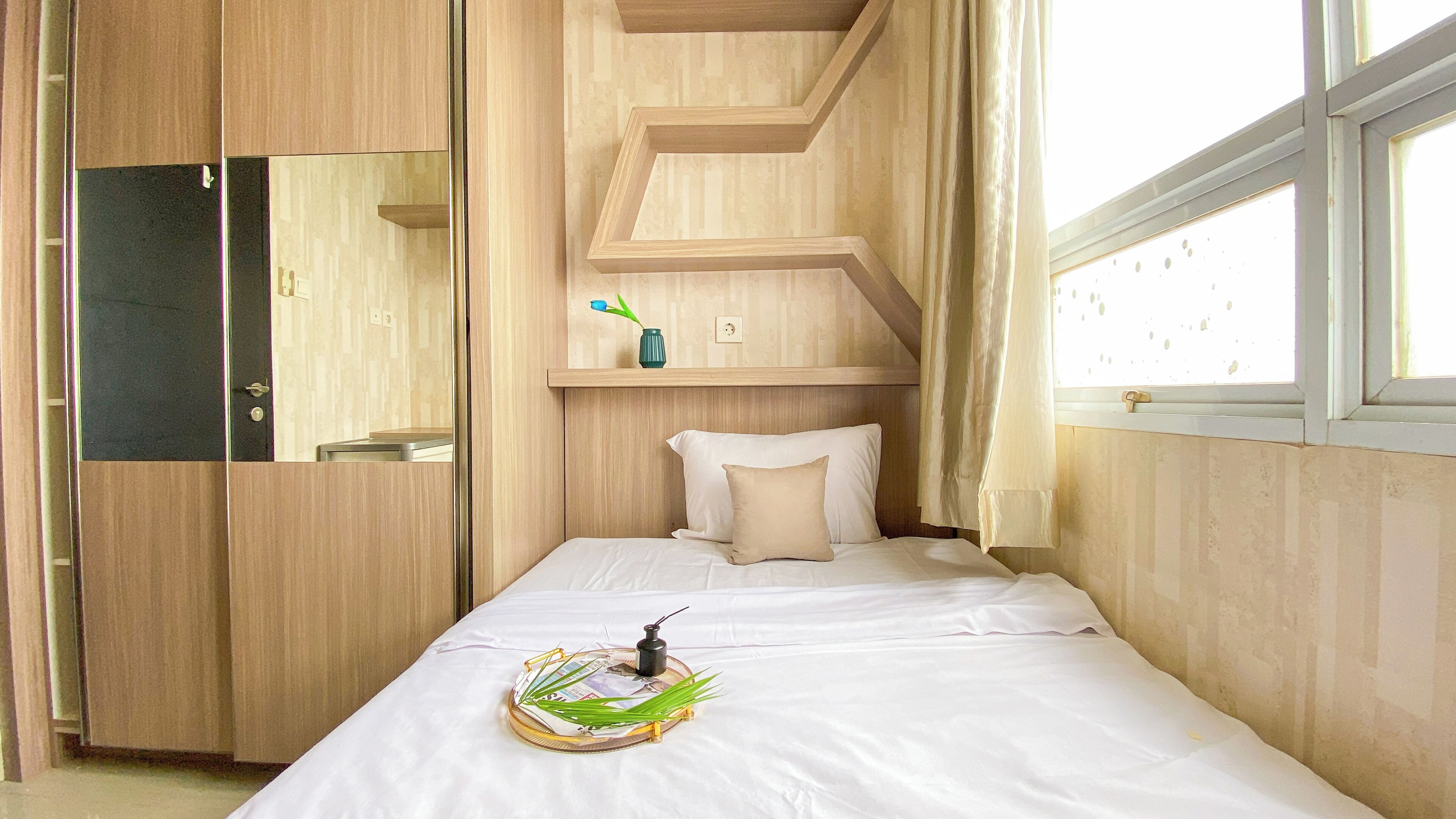 A bedroom with a bed, a mirror, a shelf with a vase, and a window.