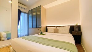 Una habitación de hotel con una cama grande, una mesita de noche con lámpara, un espejo y una ventana con cortinas.