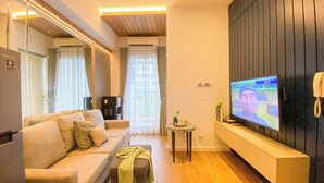 Una sala de estar moderna con un sofá, una mesa de centro, un televisor sobre un mueble, una mesita auxiliar con una planta y un espejo grande.