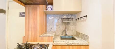 A compact kitchen with a gas stove, wooden cabinets, and a marble countertop.