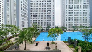Un moderno edificio de gran altura con una amplia piscina rodeada de vegetación y zonas de estar al aire libre.