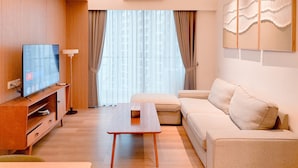A modern living room with a flat-screen TV, wooden entertainment unit, beige sofa, and a coffee table. - Spacious and Good Deal 3BR Sky House BSD Apartment (Pagedangan)