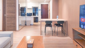 A modern hotel room with a wooden floor, a sofa, a wooden table, and a TV on a wooden stand. - Spacious and Good Deal 3BR Sky House BSD Apartment (Pagedangan)