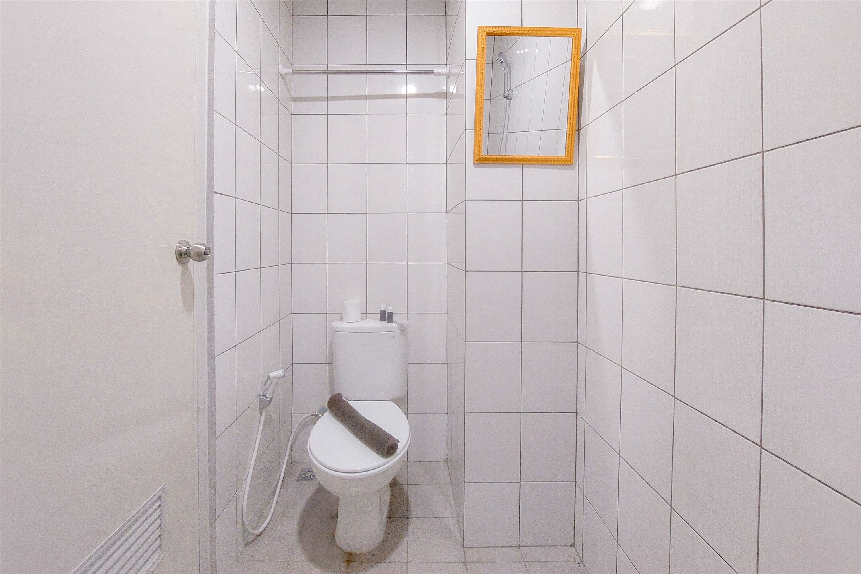 Un baño pequeño con azulejos blancos, un inodoro, un perchero y un espejo.