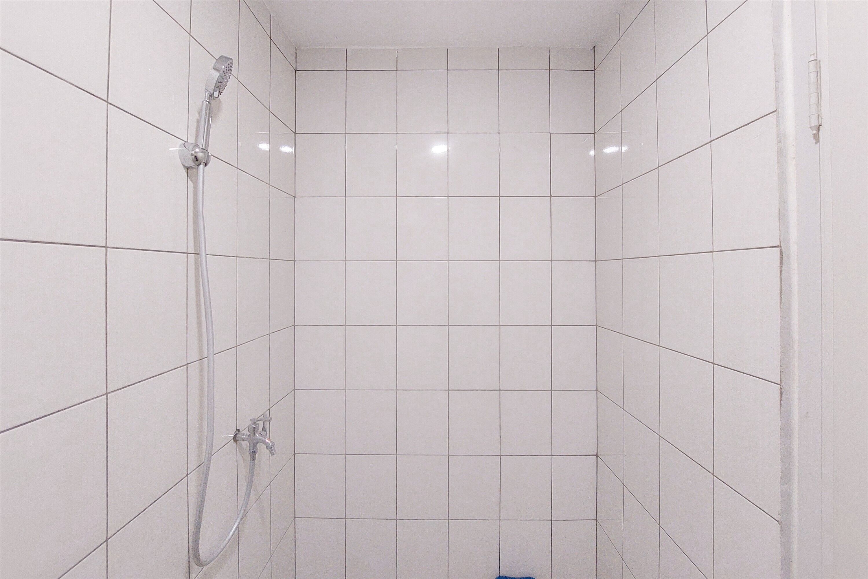 Ein Duschbereich mit Fliesen, einer Handbrause und einem am Wand montierten Wasserhahn.