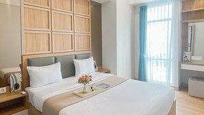 Une chambre d’hôtel moderne avec un grand lit, une tête de lit en bois, une table de chevet avec une lampe et une fenêtre avec des rideaux.