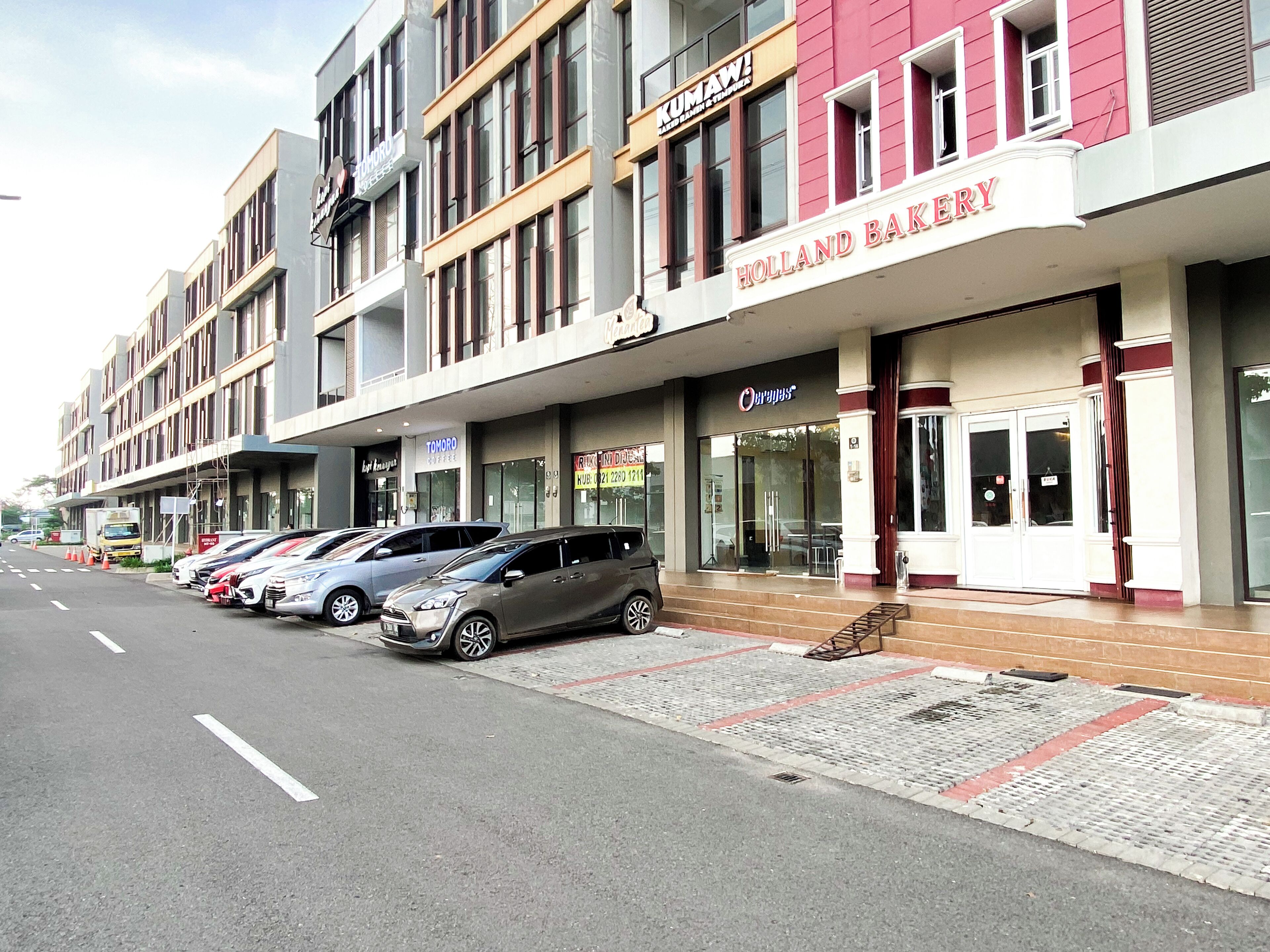Una hilera de coches aparcados frente a un edificio con un letrero que dice 'HOLLAND BAKERY'.