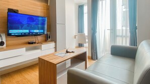 Un salon moderne avec un téléviseur à écran plat fixé à un mur en bois, un canapé blanc, une table basse en bois et une grande fenêtre ornée de rideaux bleus.