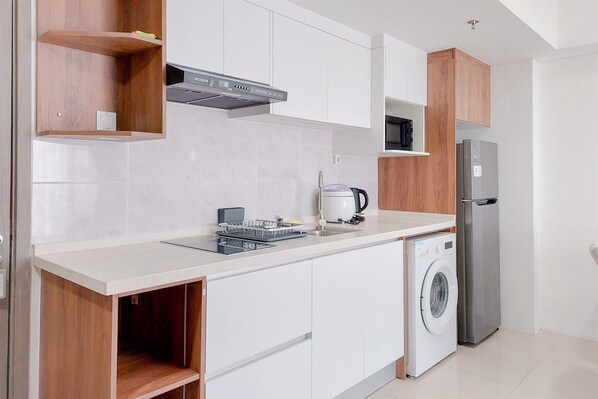 Una cocina moderna con armarios blancos, un refrigerador de acero inoxidable, lavadora integrada y un microondas.