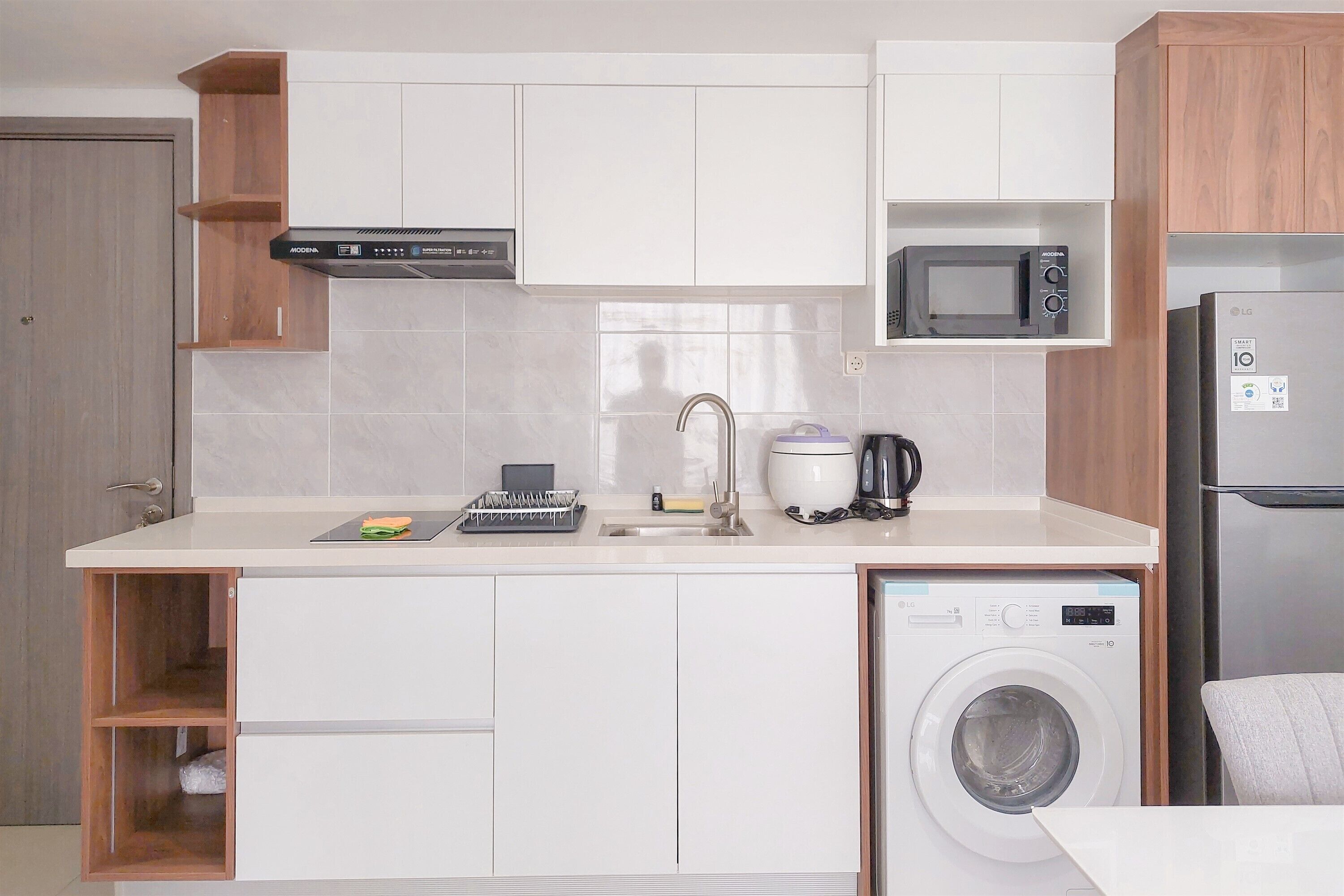 A compact kitchen with white cabinets, a microwave, a washing machine, and a coffee maker.