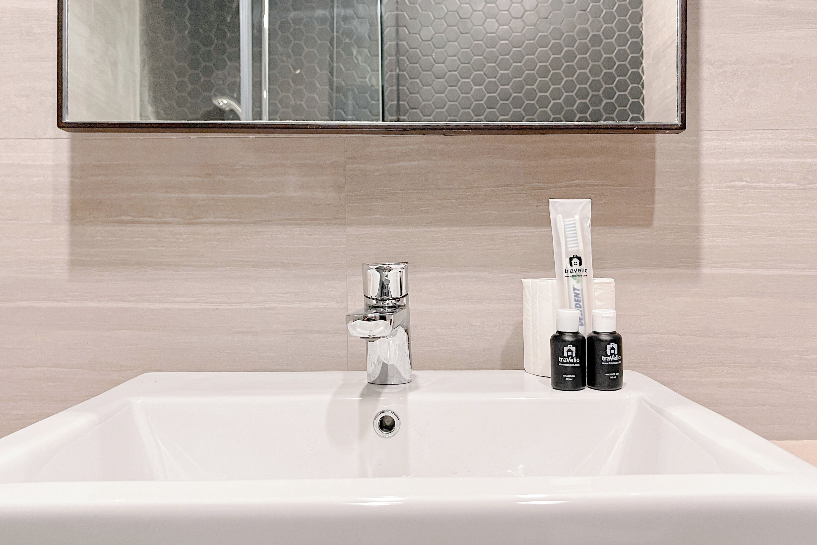 A bathroom sink with a chrome faucet, a mirror above it, and two toiletry bottles on the sink.
