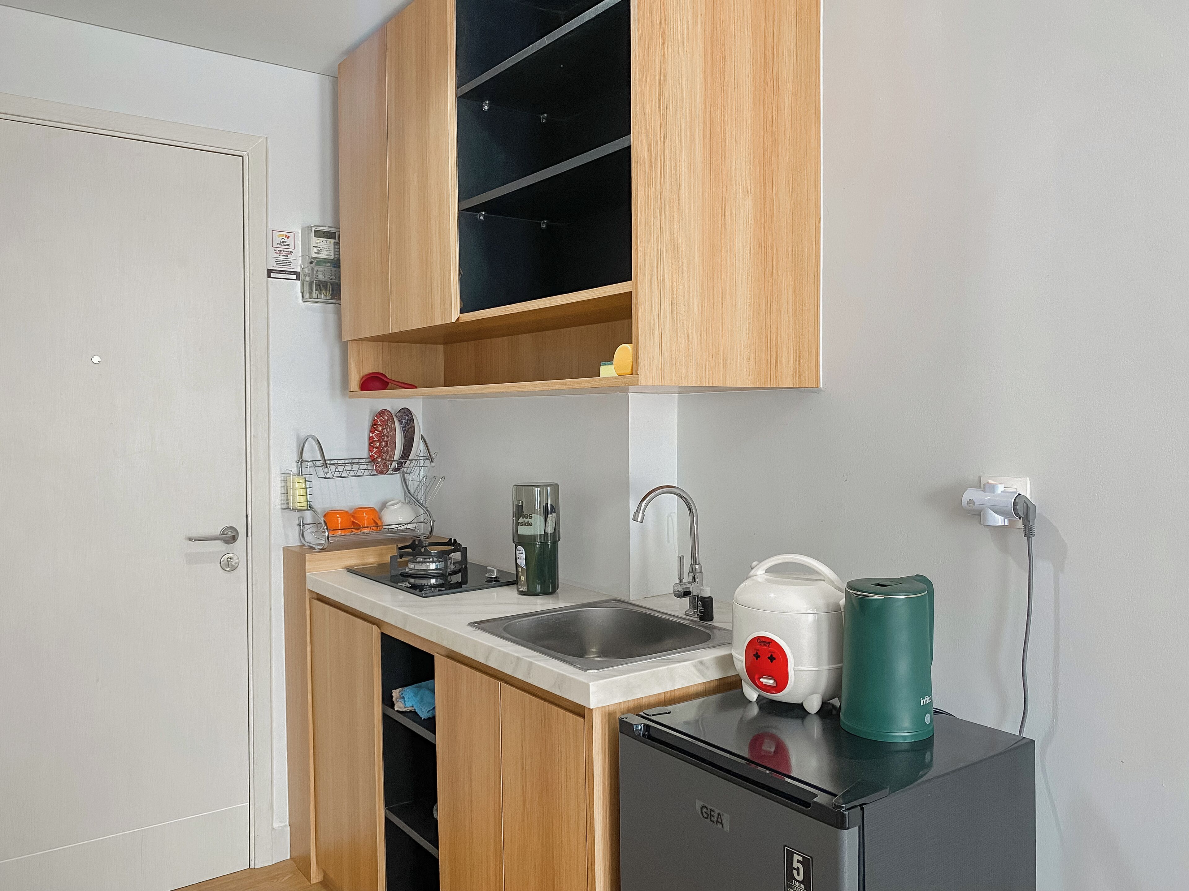 A compact kitchen with wooden cabinets, a sink, a compact refrigerator, and a kettle.